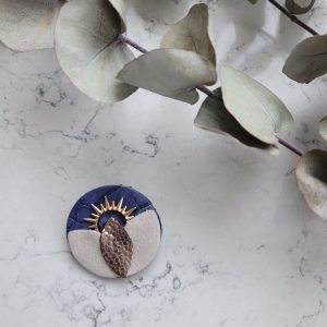 Broche solaire dnas les coloris bleu et écru e, cuir et en plaqué or